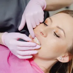 Dentysta w różowych rękawiczkach bada zęby pacjentki, która odczuwa, jak boli kieszonka dziąsłowa.