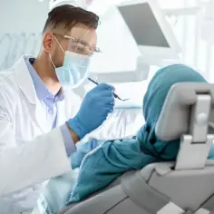 Lekarz stomatolog w masce i fartuchu bada pacjentkę w fotelu. Nawet przy łagodnym podejściu, dentofobia może być trudna do pokonania.