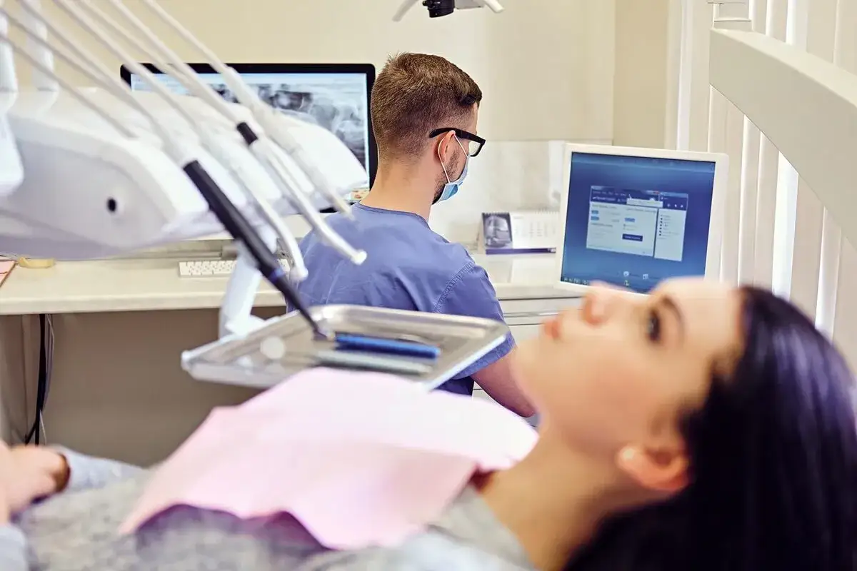 Pacjentka u dentysty, zastanawia się, czy dentysta może wystawić L4. W tle widać sprzęt stomatologiczny i monitory.