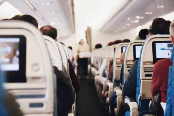Wnętrze samolotu, pasażerowie siedzą w rzędach. Czy po wyrwaniu zęba można lecieć samolotem? Zależy od zaleceń lekarza.