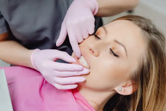 Dentysta w różowych rękawiczkach bada zęby pacjentki, która odczuwa, jak boli kieszonka dziąsłowa.